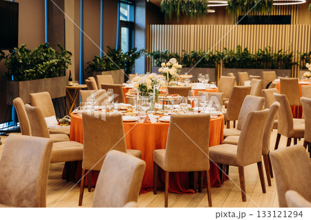 Elegant banquet hall with round tables, floral centerpieces and orange tablecloths Elegant banquet hall with round tables, floral centerpieces and orange tablecloths 133121294