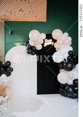 Modern birthday photo zone with black and white balloon arch and Happy Birthday neon sign 133121301