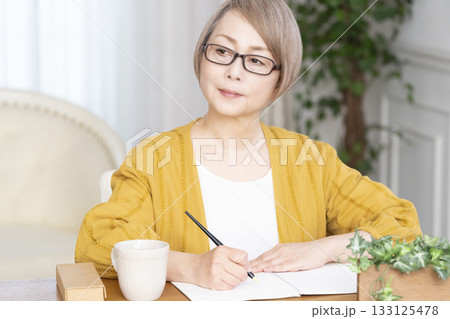 リビングでエンディングノートを書くシニア女性 133125478
