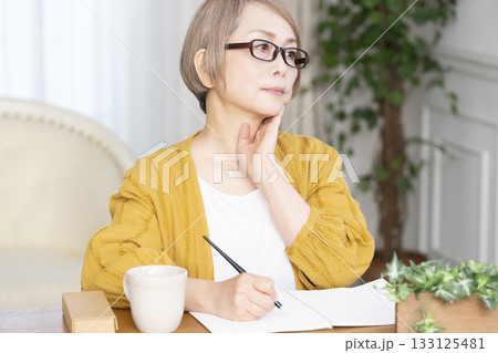 リビングでエンディングノートを書くシニア女性 133125481