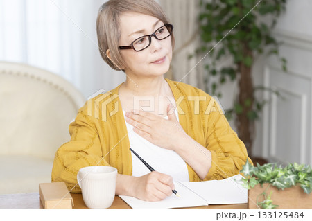 リビングでエンディングノートを書くシニア女性 133125484
