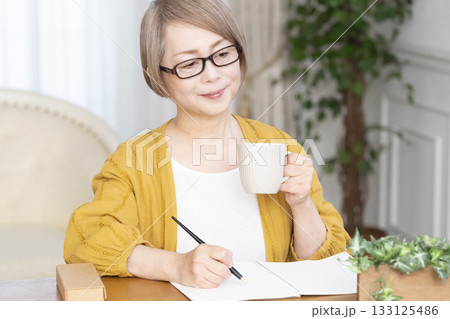 リビングでエンディングノートを書くシニア女性 133125486