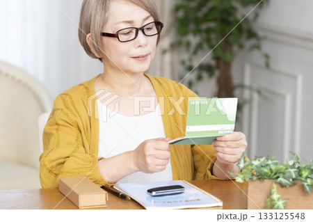 リビングでエンディングノート,通帳を見るシニア女性 133125548