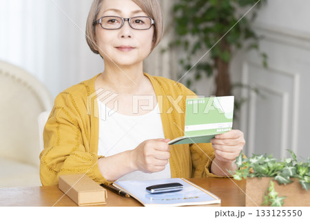 リビングでエンディングノート,通帳を見るシニア女性 133125550