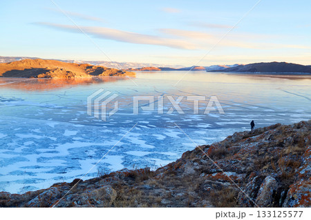 Frozen Lake Baikal. A view of clear ice surrounded by a picturesque, rolling landscape Frozen Lake Baikal. A view of clear ice surrounded by a picturesque, rolling landscape 133125577