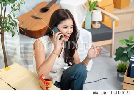 Moving Home. Young woman on phone during home relocation, smiling and organizing her new space. Moving Home. Young woman on phone during home relocation, smiling and organizing her new space. 133126120