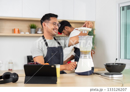 Man Using Blender. Happy man preparing a smoothie in a modern kitchen. 133126207