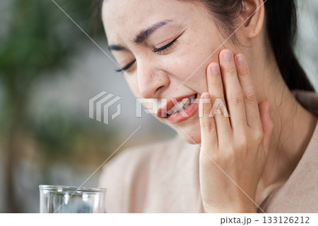 Dental Pain and Discomfort. A woman grimacing while holding her jaw, indicating tooth pain. Dental Pain and Discomfort. A woman grimacing while holding her jaw, indicating tooth pain. 133126212
