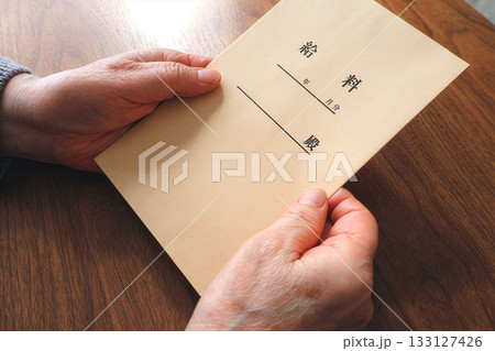 机上で給料袋を持つシニア女性の手元 机上で給料袋を持つシニア女性の手元 133127426