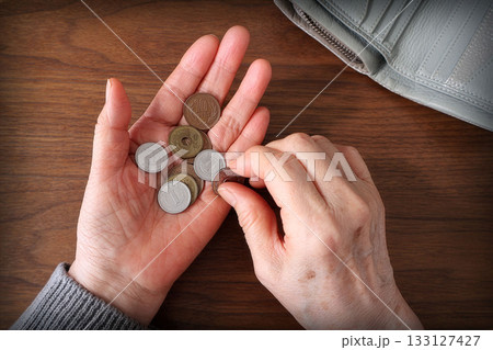 手の平の小銭を数える高齢女性の手と机上の財布 手の平の小銭を数える高齢女性の手と机上の財布 133127427