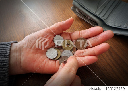 手の平の小銭を数える高齢女性の手と机上の財布 133127429