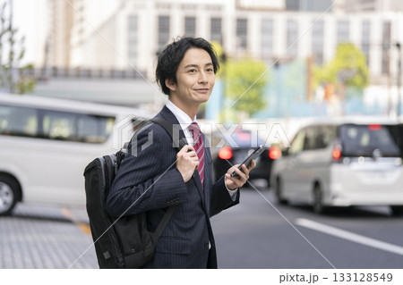 街角に立つスマートフォンを持ったビジネスマン 街角に立つスマートフォンを持ったビジネスマン 133128549