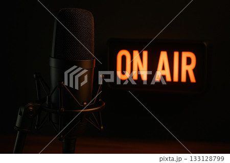 Professional podcast microphone ready for live broadcast in dark studio. glowing orange ON AIR sign creates focused and intense communication atmosphere Professional podcast microphone ready for live broadcast in dark studio. glowing orange ON AIR sign creates focused and intense communication atmosphere 133128799