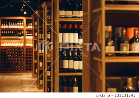 Modern wine cellar fulled various wine bottles, close up photography. Long corridor with wooden shelves fulled bottles of elite wine in cellar of alcohol store. Modern wine cellar fulled various wine bottles, close up photography. Long corridor with wooden shelves fulled bottles of elite wine in cellar of alcohol store. 133131243