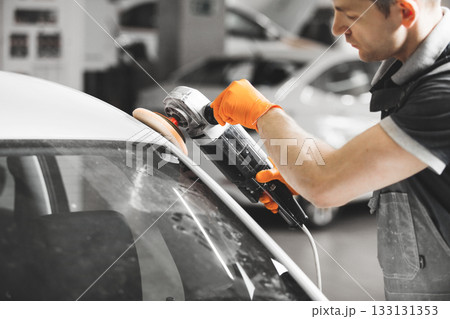 Worker polished white car with orbital polisher in auto repair shop, close-up. Vehicle detailing. 133131353