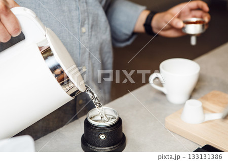 Pouring Boiling Water From Electric Kettle Into an Italian Coffee Makers Tank Pouring Boiling Water From Electric Kettle Into an Italian Coffee Makers Tank 133131386