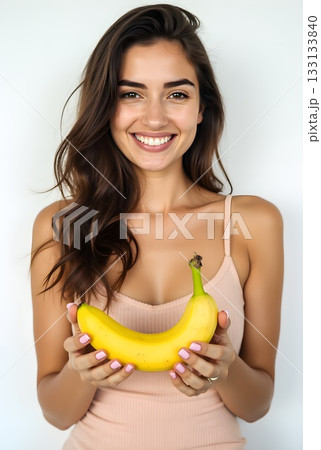 Smiling woman holding a ripe banana in a bright indoor setting with a neutral background 133133840