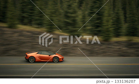 Low-profile orange sports car is racing along a 133136207