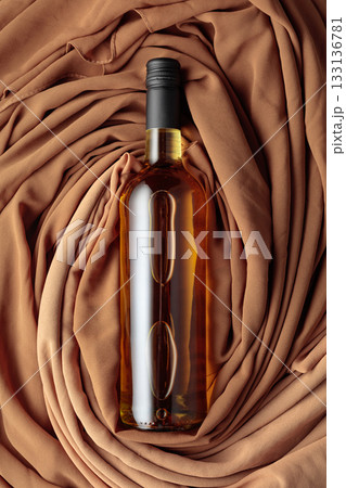 Bottle of white wine against a background of draped beige and brown fabric. 133136781