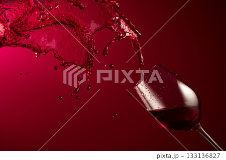 Glass and red wine splash on a dark red background. 133136827