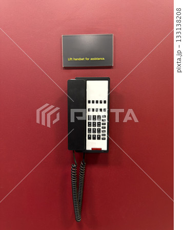 Vertical photo of black telephone on red wall. Concept of landline telephone communication. Warning sign Lift handset for assistance to speak to operator. Quick way to contact operator Vertical photo of black telephone on red wall. Concept of landline telephone communication. Warning sign Lift handset for assistance to speak to operator. Quick way to contact operator 133138208