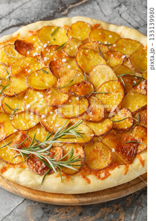 Potato and Rosemary Pizza is made with thinly sliced potatoes drizzled in olive oil and fresh rosemary and baked until crispy closeup on the wooden board. Vertical 133139980
