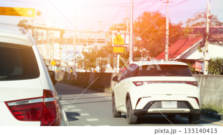 Rear side of white car driving on asphalt road. Other car drive through. High concrete road barriers side of road. blurred of house and trees with pole and sign board. 133140413