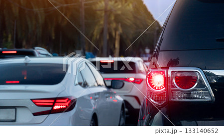 Rear side of luxury car with turn on brake light. Traffic jam on the road with many car queue. Blurred of tall trees for background. 133140652