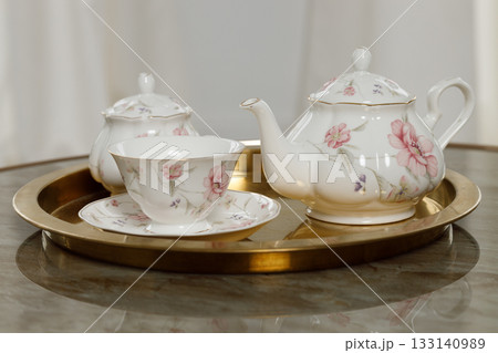 Elegant floral teapot and teacup set on a gold tray for a refined tea setting Elegant floral teapot and teacup set on a gold tray for a refined tea setting 133140989