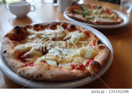 ふっくら焼き上がったピザ二皿が並ぶ食卓 ふっくら焼き上がったピザ二皿が並ぶ食卓 133142296