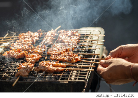Vendor selling junk food, grilling chicken on sticks on homemade grill for customers outdoors. Vendor selling junk food, grilling chicken on sticks on homemade grill for customers outdoors. 133143210