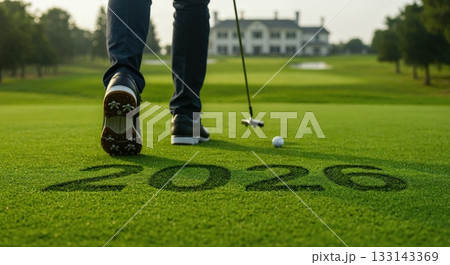 An immersive low-angle shot captures a person's legs and golf shoes striding on a green putting surface, with the year 2026 mown into the turf, a golf ball, and a distant clubhouse. 133143369