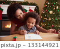 Smiling African American 6 years old boy with her mom writing dear Santa letter in his room with Christmas decoration. 133144921