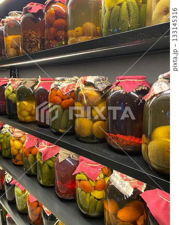 Preserved fruits and vegetables in big jars lined up on black wooden shelves Preserved fruits and vegetables in big jars lined up on black wooden shelves 133145316