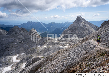 Hiker walking through dry alpine landscape with rocky peaks and no foliage, Slovenia Hiker walking through dry alpine landscape with rocky peaks and no foliage, Slovenia 133145377