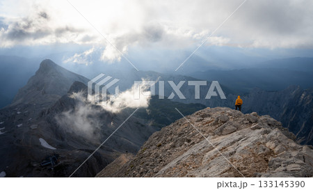 Hiker standing on top of a mountain enjoying view on beautiful alpine landscape ahead, Slovenia Hiker standing on top of a mountain enjoying view on beautiful alpine landscape ahead, Slovenia 133145390