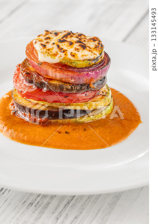 Elegant vertical ratatouille tower layered with colorful vegetables on white plate Elegant vertical ratatouille tower layered with colorful vegetables on white plate 133145493