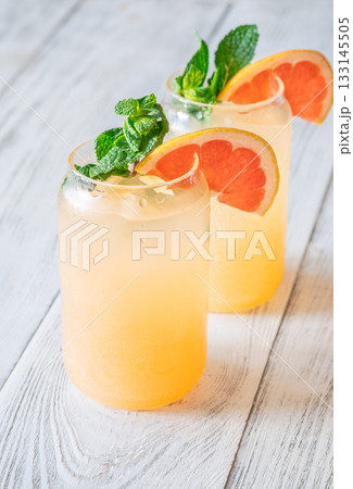 Two chilled Paloma cocktails with grapefruit slices and mint sprigs on white wood 133145505
