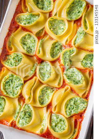 Golden baked lumaconi filled with ricotta and spinach resting in rich tomato sauce 133145548