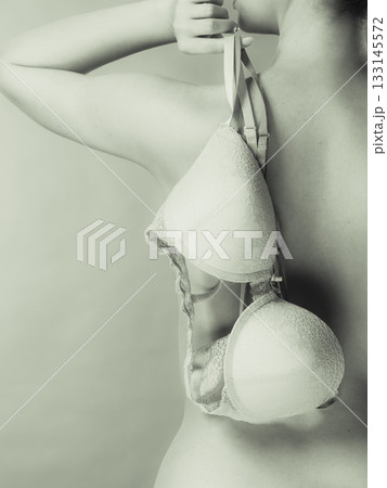 Naked woman holds beige bra in hand 133145572