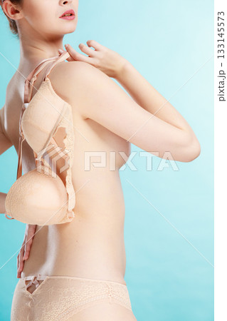Naked woman holds beige bra in hand Naked woman holds beige bra in hand 133145573