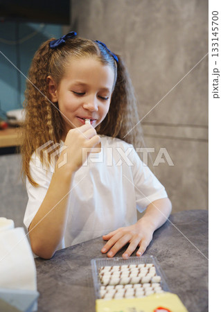 Girl enjoying candy while sitting at kitchen table in cozy home setting 133145700