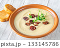 Terracotta bowl of creamy cauliflower soup paired with toasted baguette on bright wooden surface 133145786