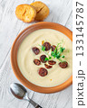 Terracotta bowl of creamy cauliflower soup paired with toasted baguette on bright wooden surface 133145787