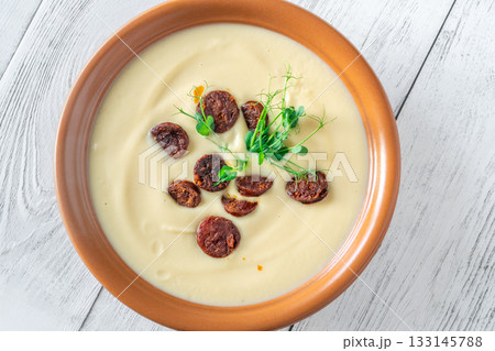 Creamy cauliflower soup with spicy chorizo served warmly in terracotta bowl on white table 133145788