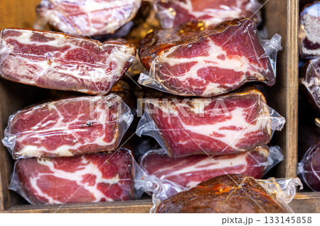 Vacuum-sealed cured meat pieces form layered stacks with rich marbling and deep color. market display shows texture, freshness and artisanal quality of traditional delicacy 133145858