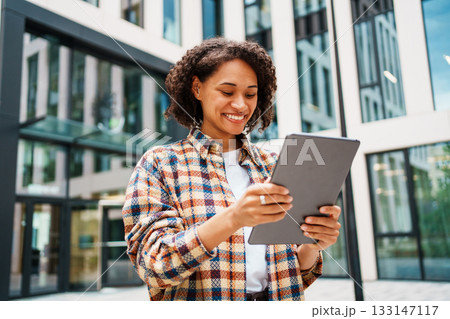 A Young Woman Utilizing a Tablet While Enjoying the Outdoors in a Modern, Urban Setting A Young Woman Utilizing a Tablet While Enjoying the Outdoors in a Modern, Urban Setting 133147117