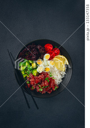 Fresh poke bowl with tuna, avocado, and vegetables served on a black plate Fresh poke bowl with tuna, avocado, and vegetables served on a black plate 133147358