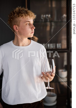 Informal portrait of blond man holding glass in sleek kitchen Informal portrait of blond man holding glass in sleek kitchen 133147713