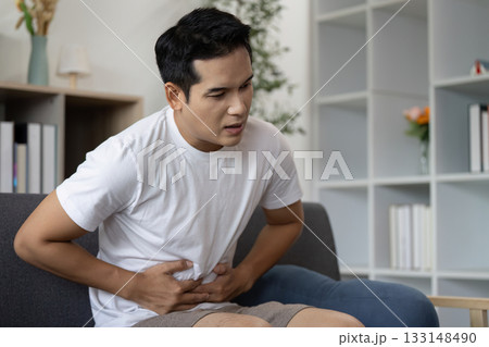 Abdominal Pain. Young man experiencing discomfort while sitting at home. Abdominal Pain. Young man experiencing discomfort while sitting at home. 133148490